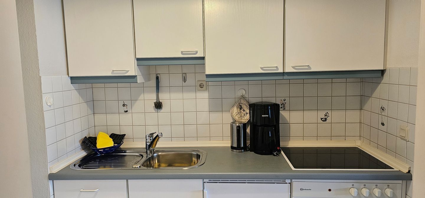 Eine Küche mit weißen Schränken, einer Edelstahl-Spüle, einer schwarzen Kaffeemaschine und einem Herd.