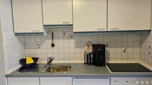 Une cuisine avec des meubles blancs, un évier en acier inoxydable, une machine à café noire et une cuisinière.