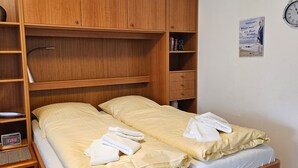 Une chambre avec deux lits, des étagères en bois, une horloge et une affiche au mur.