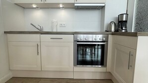 A compact kitchen with white cabinetry, a built-in oven, and a coffee maker on the countertop.