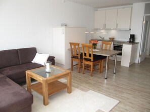 A modern living room with a brown sofa, a glass coffee table, and a dining area with wooden chairs and a table. - Apartment Deckerstrasse 19-21 App. 17 - 3 room apartment in Deckerstr. (Sylt)