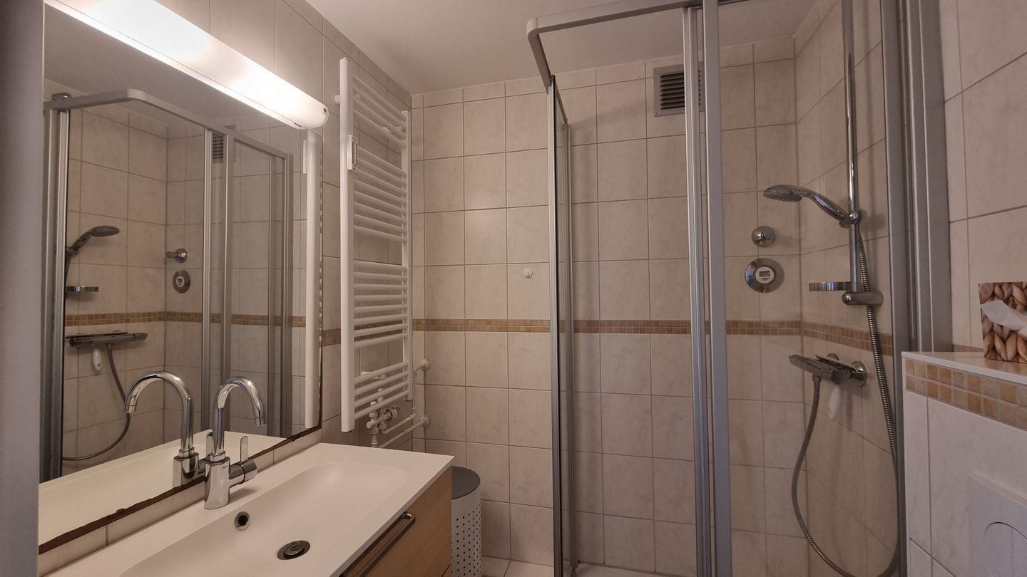Een moderne badkamer met een douche met glazen wand, een wastafel met spiegel en een handdoekrek.