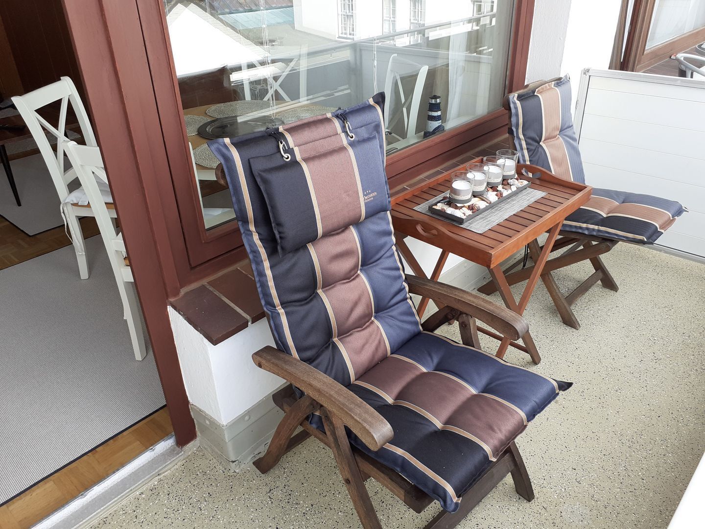 A sunlit outdoor seating area with a wooden table and two cushioned chairs.