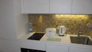 Una cocina compacta con horno integrado, cafetera, hervidor y pileta.