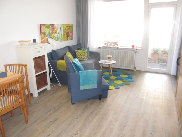 Un salon moderne avec un canapé, une chaise en bois, une petite table et un tapis coloré.