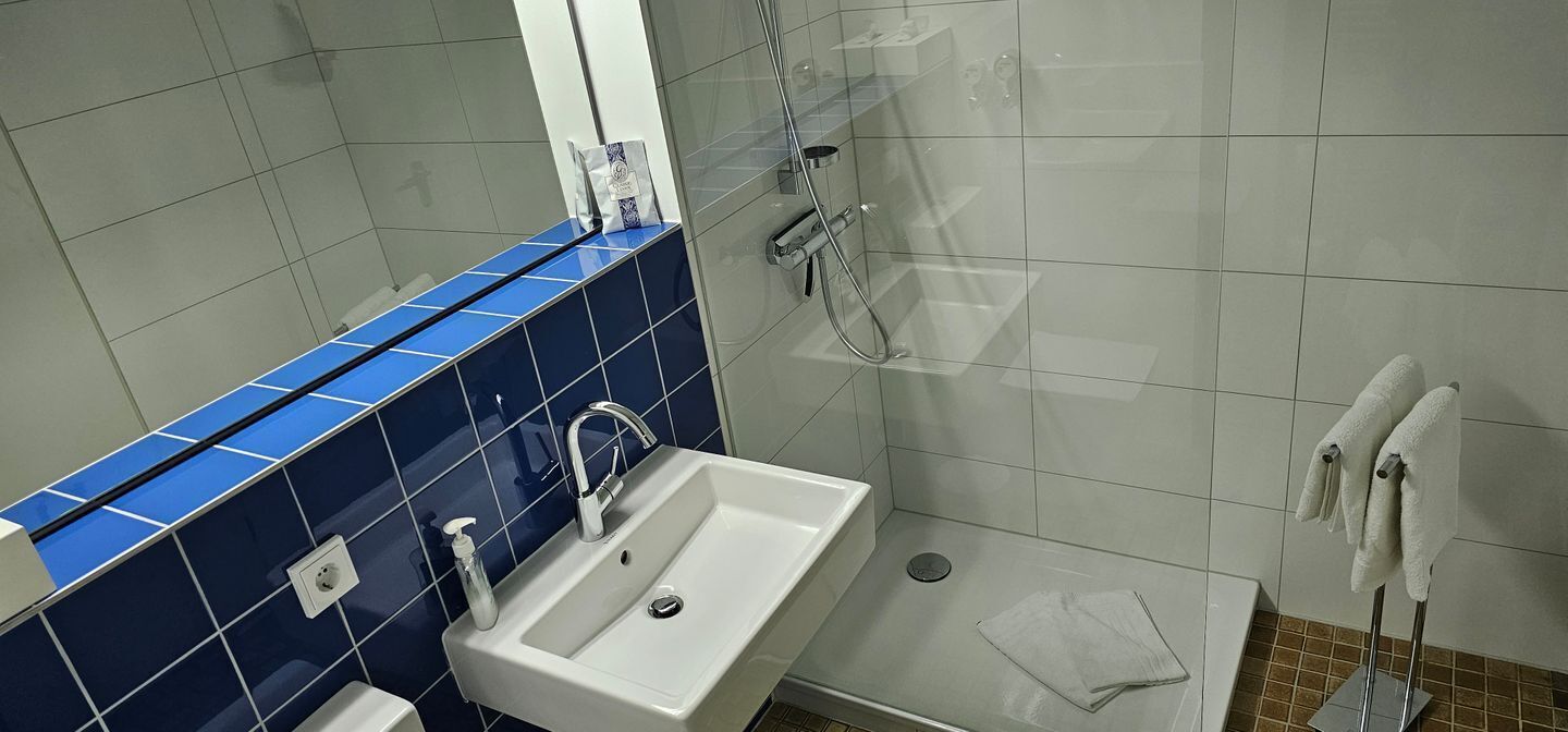 A bathroom with a white sink, blue-tiled wall, and a glass shower enclosure.