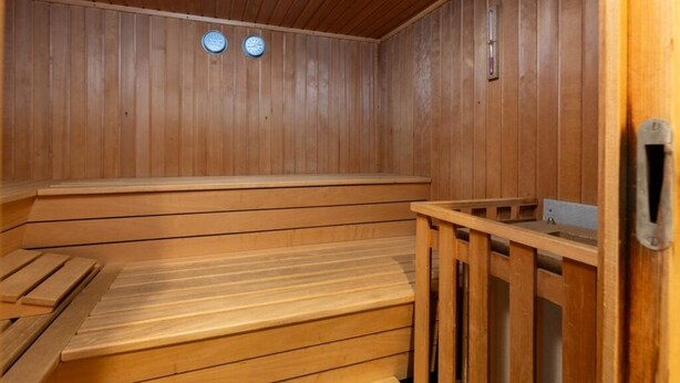 Una sauna de madera con bancos y un asiento de banco, una puerta de madera y una ventana pequeña.