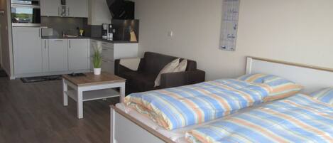 A compact room with a bed, a sofa, a small table, and a kitchenette.