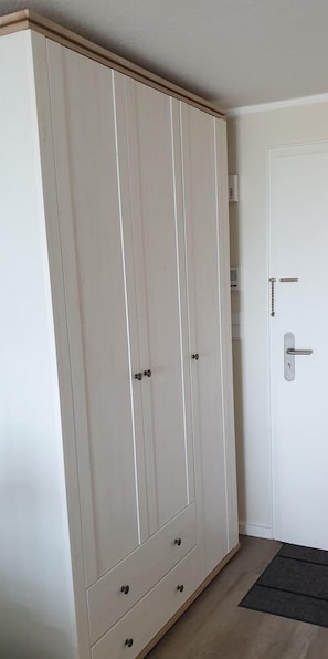 A white wardrobe with two doors and a small drawer, a white door with a handle, and a black doormat.