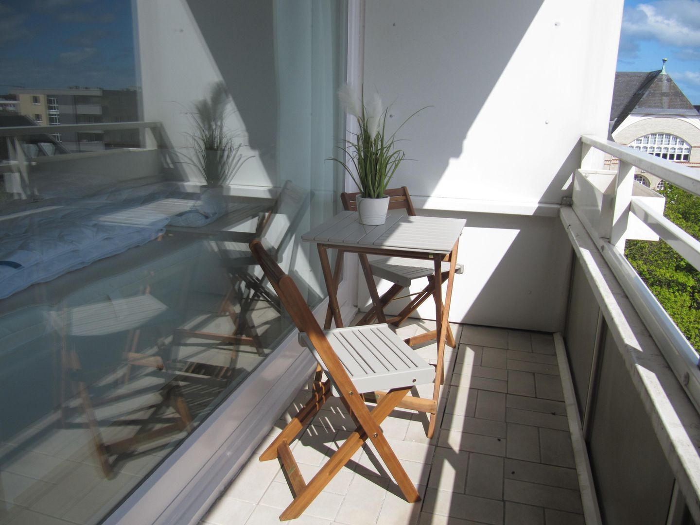A balcony with a wooden table and chairs, a potted plant, and a view of the sea.