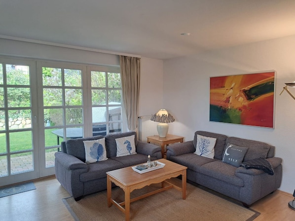A living room with two grey sofas, a wooden coffee table, a lamp, and a colorful abstract painting on the wall. - Halemdüür 9 An Apartment No. 1 - 3 room apartment in the south of Westerland. (Sylt)