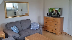 A living room with a sofa, a wooden coffee table, a TV on a wooden dresser, and a mirror on the wall. - Halemdüür 9 An apartment no. 2 - 2 room apartment in the south of Westerland. (Sylt)