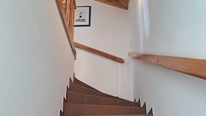 A staircase with brown tiles and wooden handrails, leading to a landing with a framed picture. - Halemdüür 9 An apartment no. 2 - 2 room apartment in the south of Westerland. (Sylt)