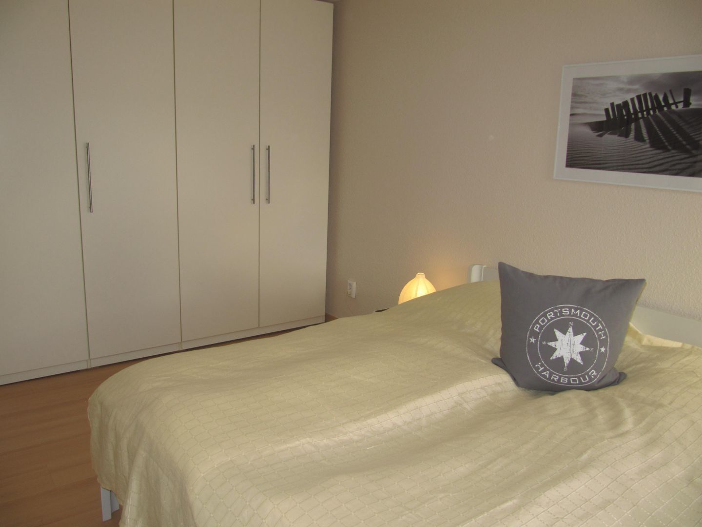 A bedroom with a bed, a wardrobe, a lamp, and a pillow with a logo.