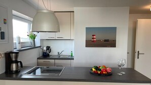A modern kitchen with a built-in stove, a coffee maker, and a fruit bowl with wine glasses.