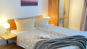 A bedroom with a bed, nightstands, a wooden wardrobe, and a painting on the wall.