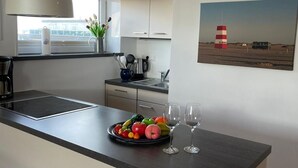A modern kitchen with a central island, a large window, and a painting of a lighthouse on the wall.