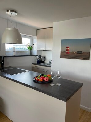 Une cuisine moderne avec un îlot central, une grande fenêtre et un tableau représentant un phare accroché au mur.