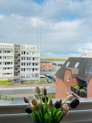 Ein modernes Mehrstöckiger Bau mit großen Fenstern, eine Straße mit parkenden Autos und Blick aufs Meer.
