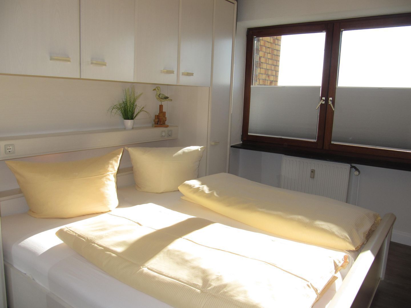 A bedroom with a bed, white walls, a window, and a radiator.