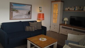 Een woonkamer met een blauwe bank, een houten salontafel, een televisie en een boekenkast.