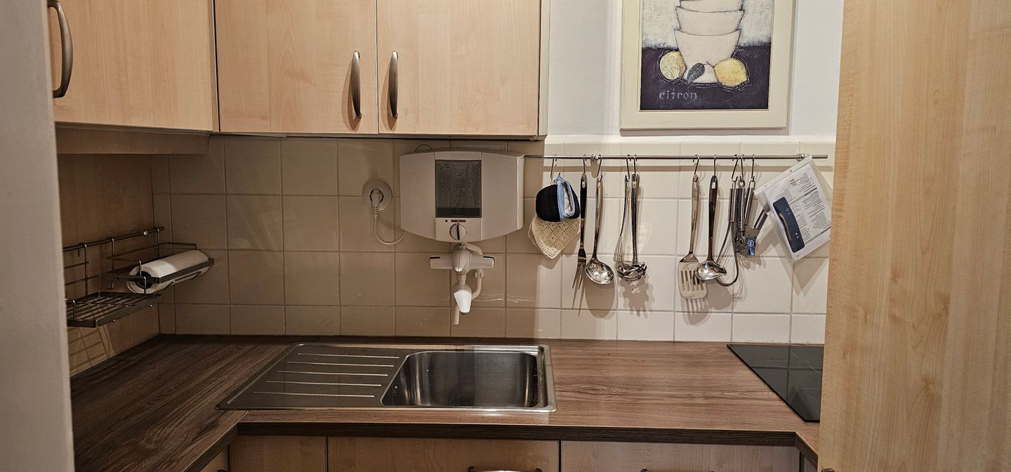 Una cocina con armarios de madera, un lavamanos de acero inoxidable y un grifo instalado en la pared.