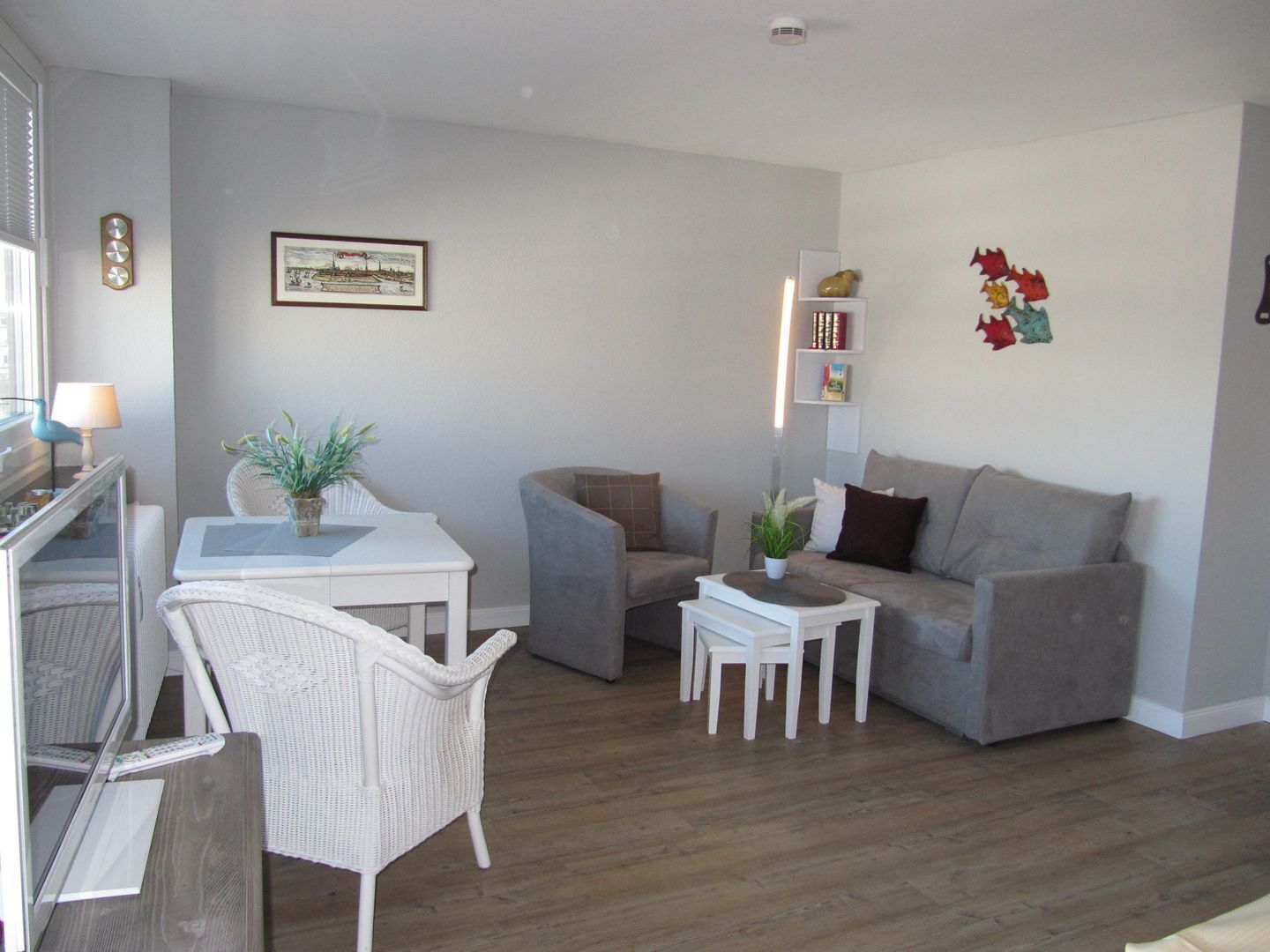 Ein modernes Wohnzimmer mit einem grauen Sofa, weißen Sesseln, einem kleinen Tisch und einem gerahmten Bild an der Wand.
