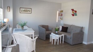Ein modernes Wohnzimmer mit einem grauen Sofa, weißen Sesseln, einem kleinen Tisch und einem gerahmten Bild an der Wand.