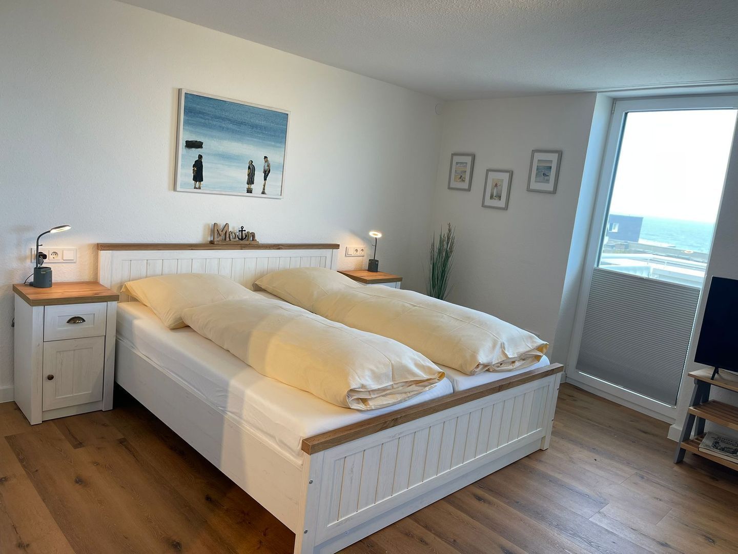 A bedroom with a bed, two bedside tables, a nightstand, a window with a view, and a painting on the wall.