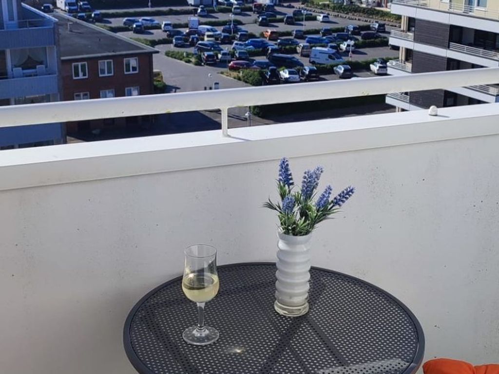 A balcony with a round table, a glass of white wine, and a vase with lavender.