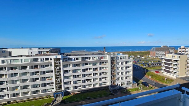 Ein Hochhaus mit mehreren Balkonen, einem Parkplatz und Blick auf das Meer.