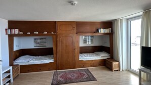 Ein Zimmer mit zwei Etagenbetten, einem Fernseher, einem kleinen Tisch und einem fenster mit Vorhängen.