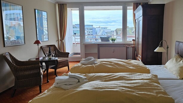 Een hotelkamer met twee bedden, een zithoek met een stoel en tafel, een raam met uitzicht op gebouwen en een kast.