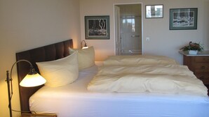 Een netjes opgemaakt bed met witte lakens, een bedlampje en een ingelijst kunstwerk aan de muur.