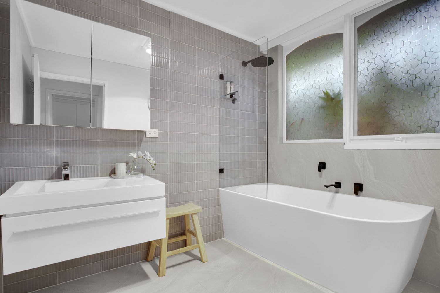 A modern bathroom with a freestanding bathtub, a vanity with a mirror, and a small stool.