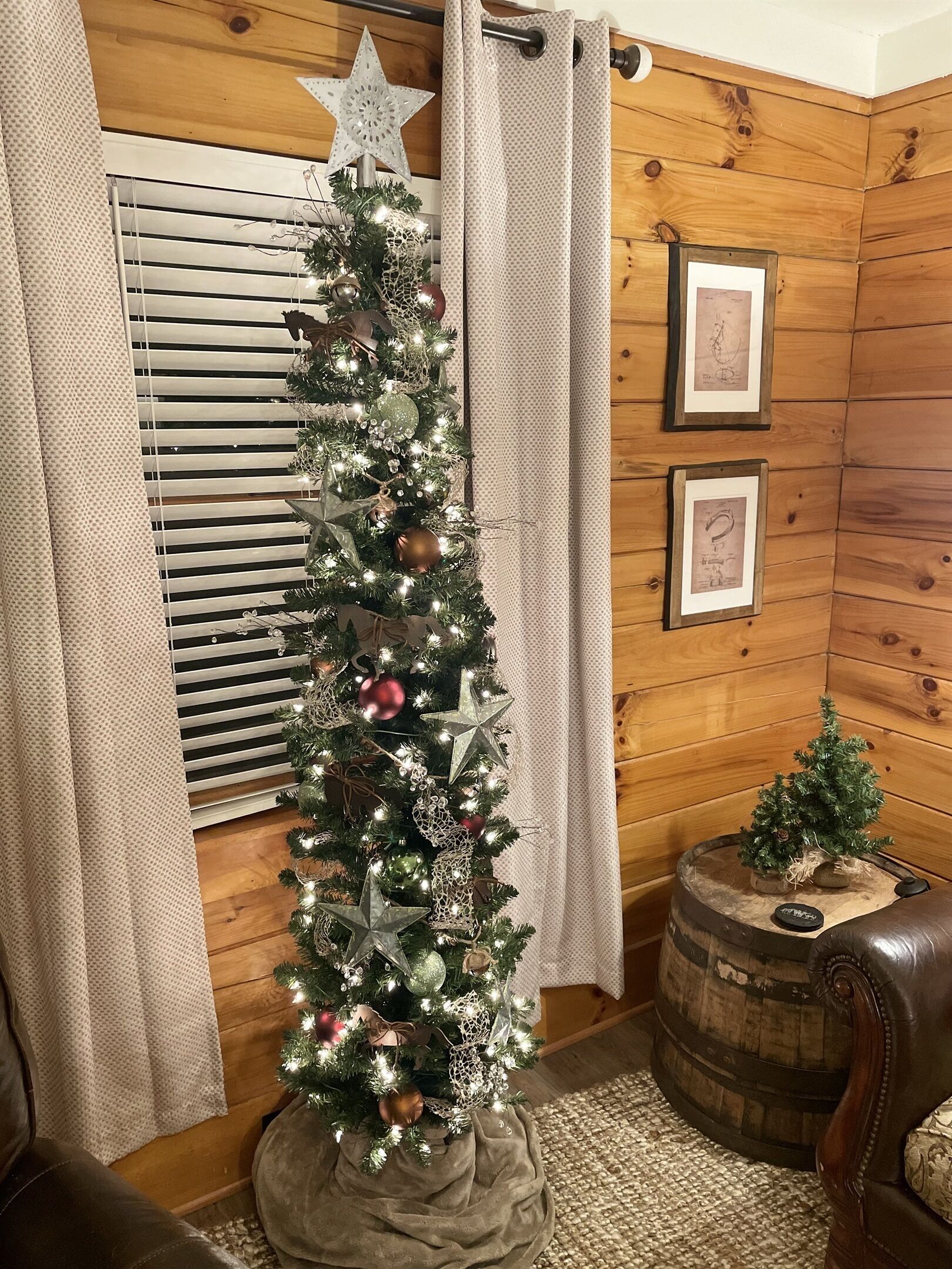 A Christmas tree in a wooden room with a window, a small table, and a leather chair.