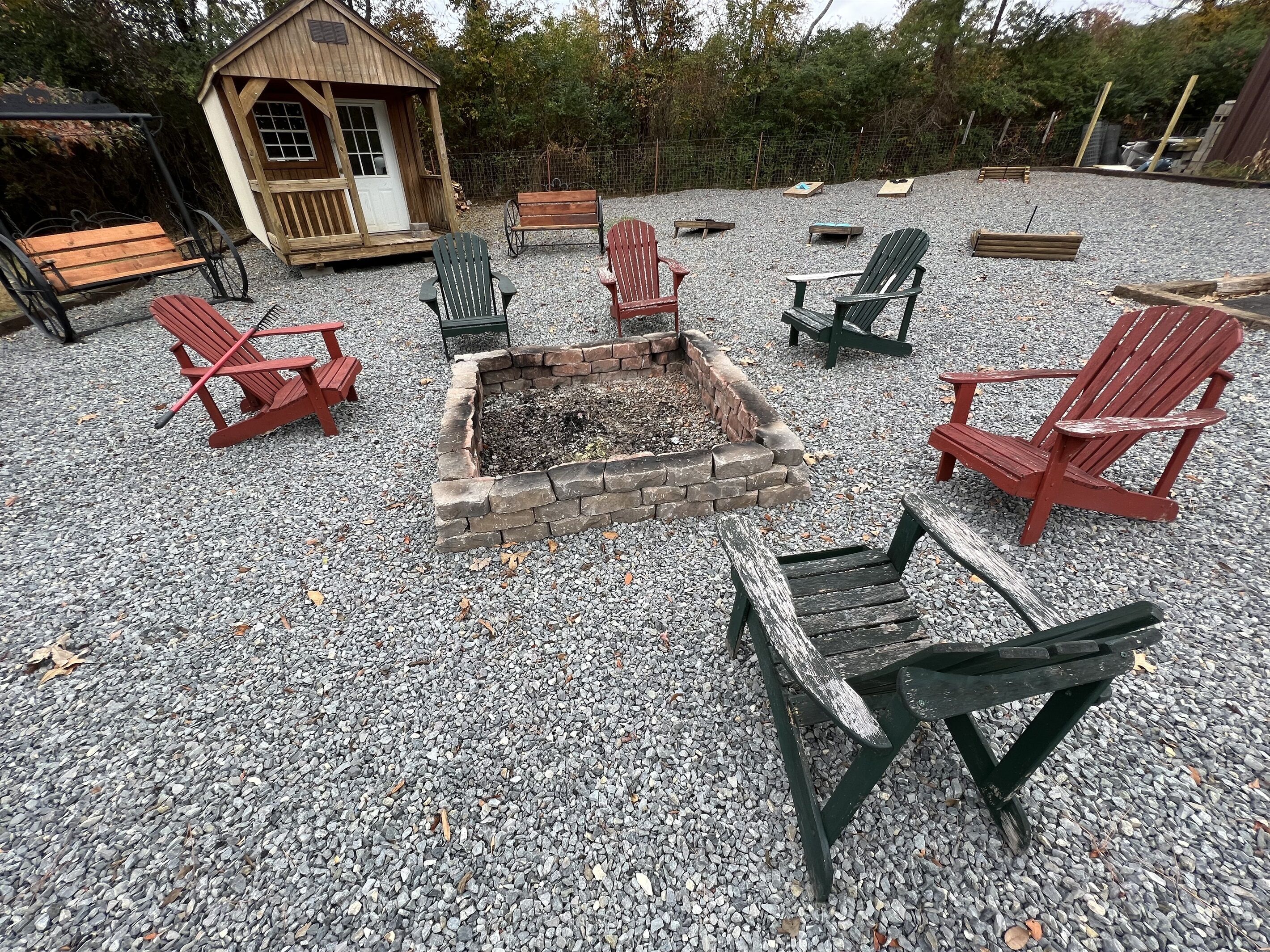 Eine Kiesterrasse mit Adirondack-Stühlen, einer Feuerstelle und einer Holzhütte.