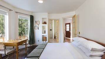 Un dormitorio con una cama grande, un escritorio de madera con un tablero de ajedrez y vistas al exterior a través de las ventanas.