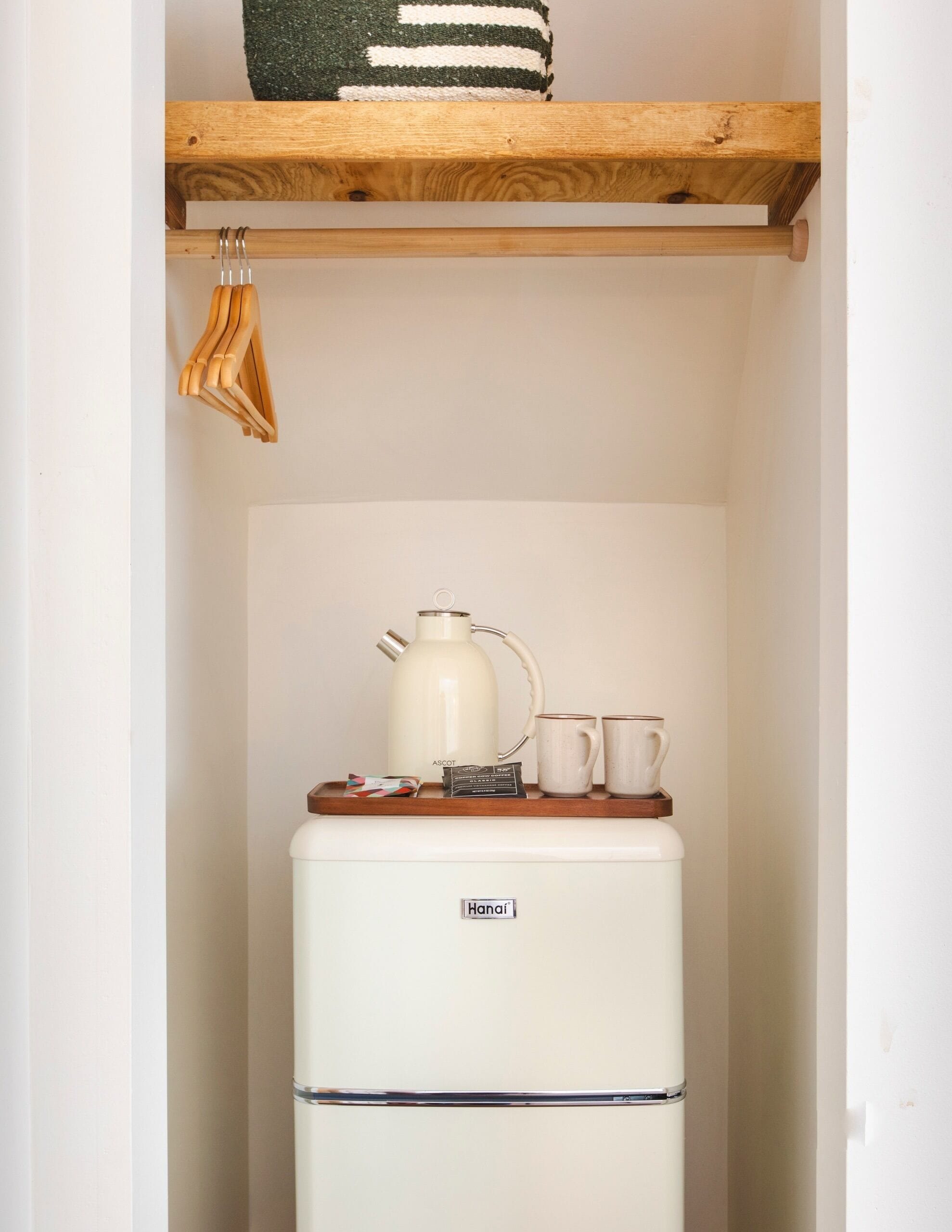 Uma cozinha compacta com geladeira branca, chaleira, duas canecas e uma prateleira de madeira acima.