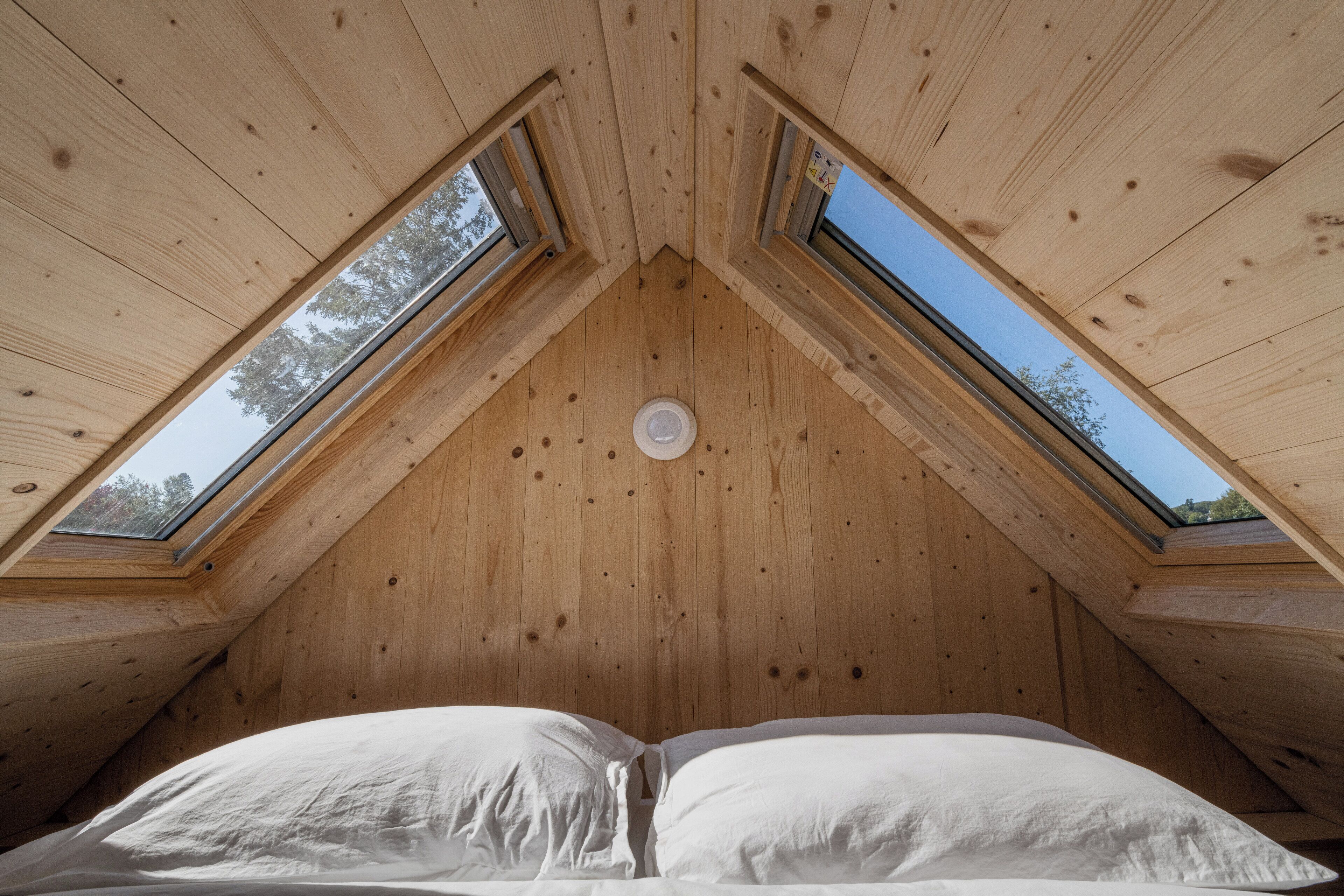 A room with a sloped ceiling and two skylights, providing natural light and a view of the sky.