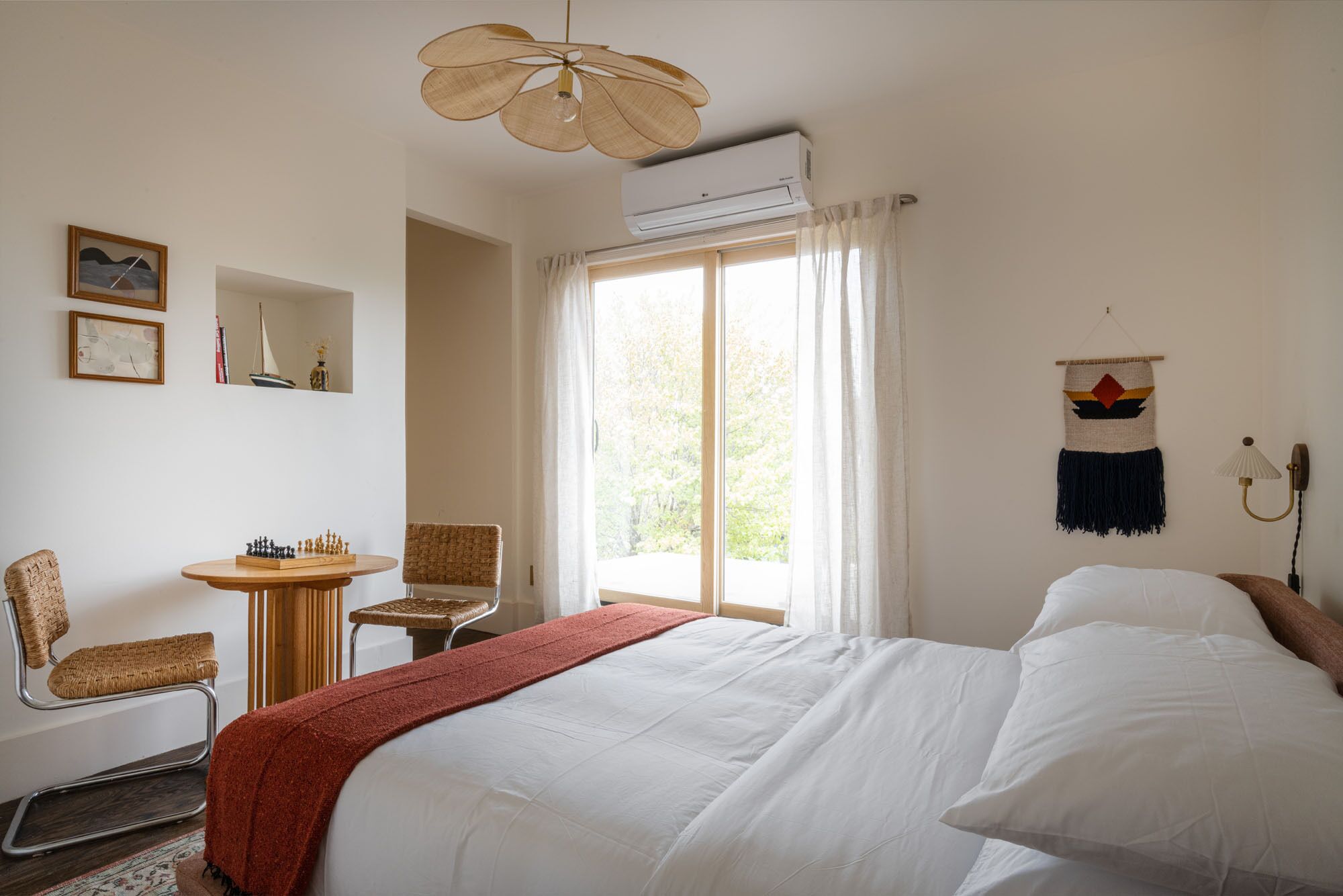 A bedroom with a bed, a chair, a small table, and a window with curtains.