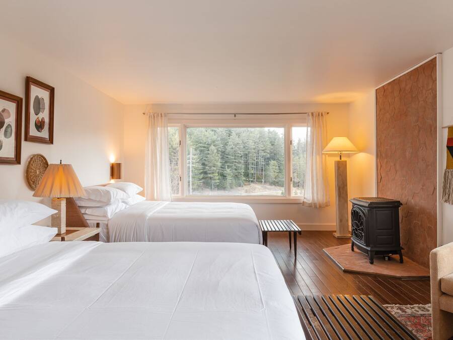 Habitació d'hotel amb dos llits, un sòl de fusta, una cuina negra, una banca i vistes a arbres a través de la finestra.