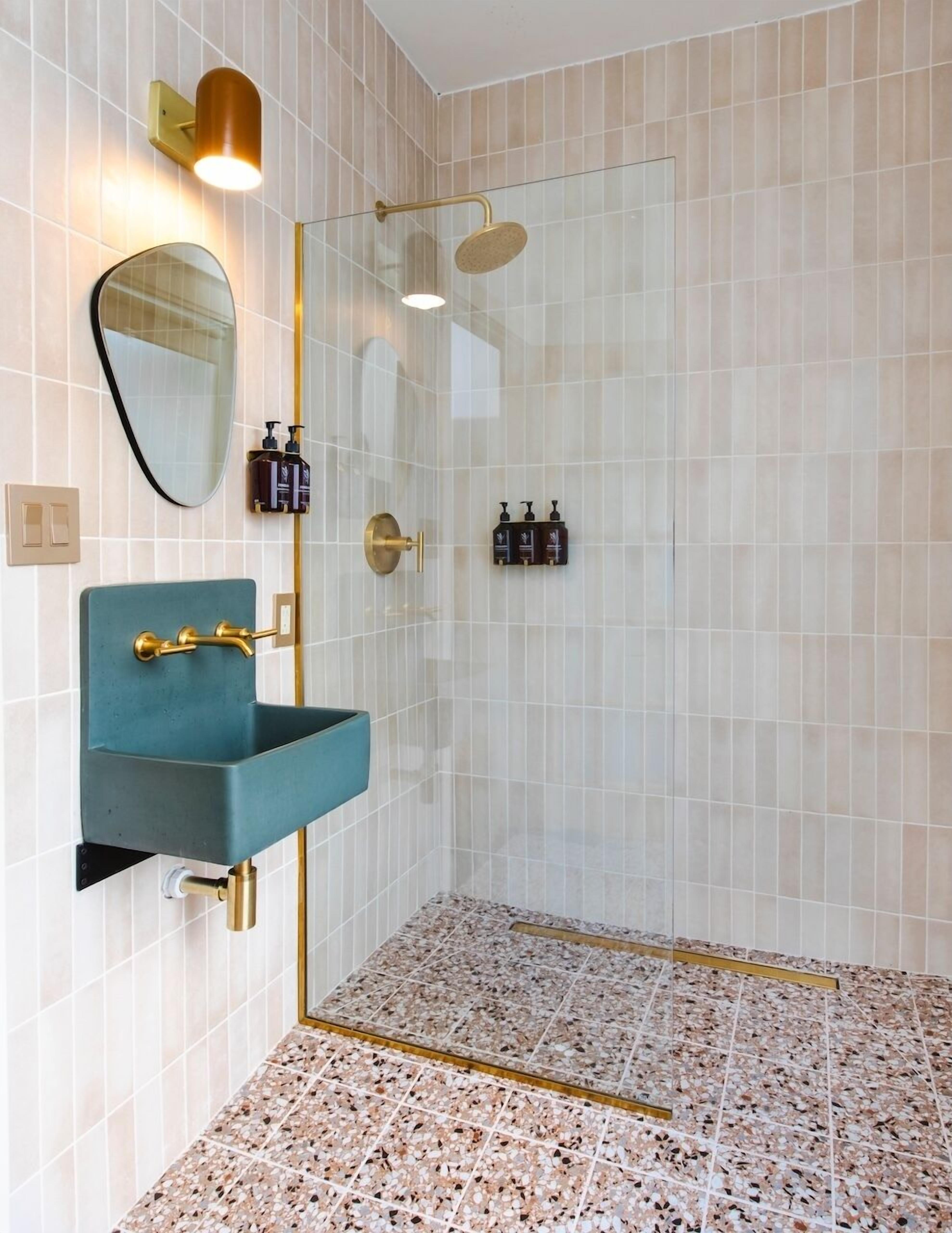 A modern bathroom with a glass shower enclosure, a teal sink with gold fixtures, and a large mirror.
