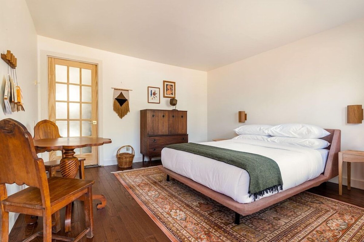 A bedroom with a bed, wooden furniture, a rug, and a door.