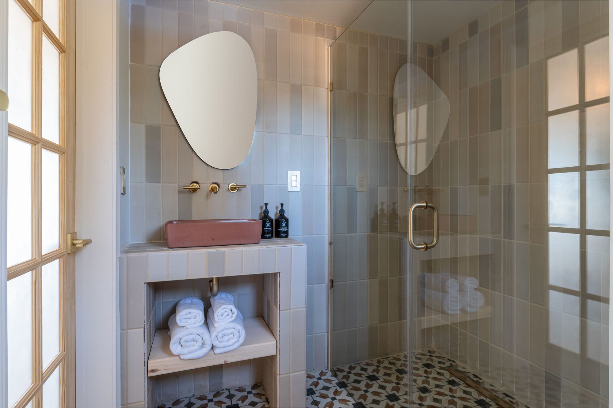 Ein modernes Badezimmer mit Waschtisch, einem großen Spiegel, einer Dusche mit Glastür und einem Musterfliesenboden.