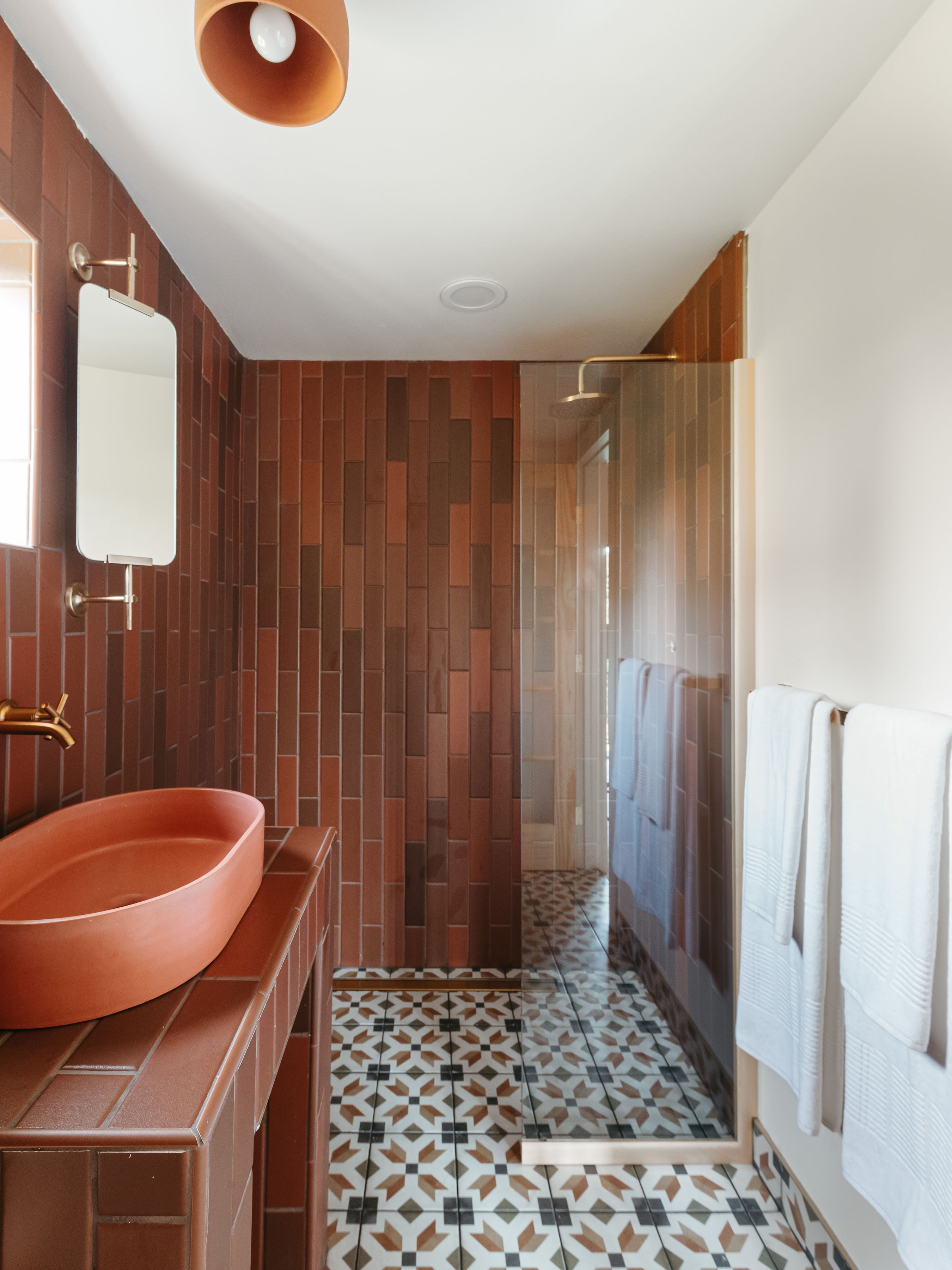A modern bathroom with a large oval sink, a mirror, a shower with a glass door, and patterned floor tiles.