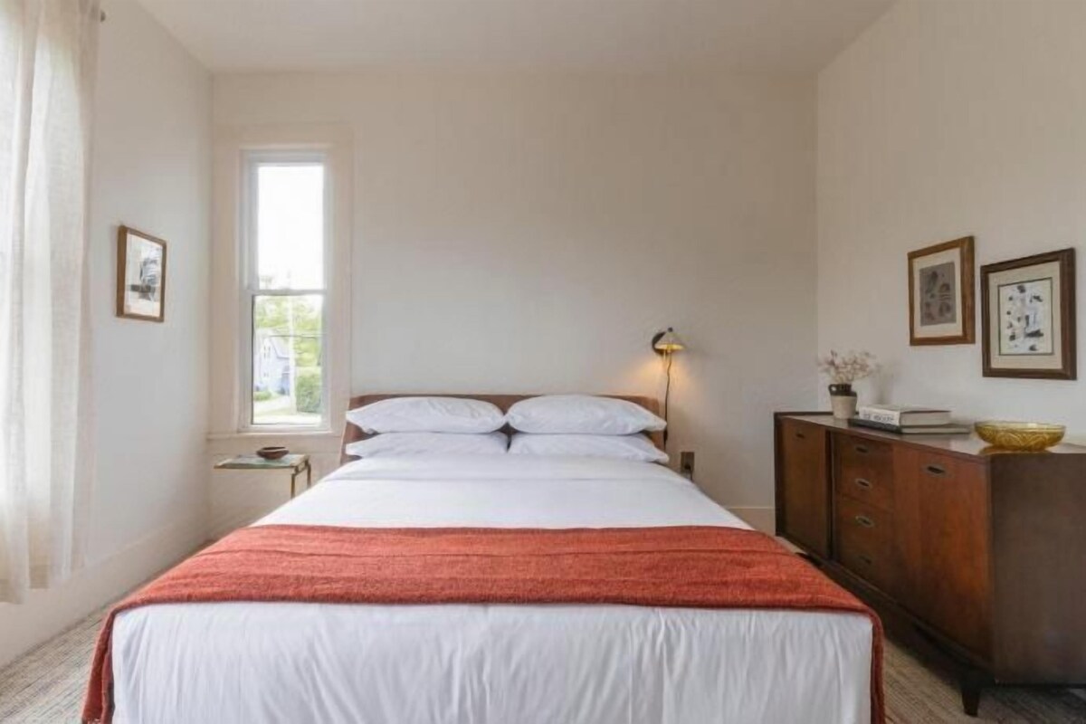 A bedroom with a bed, a nightstand, a lamp, a dresser, and a window.