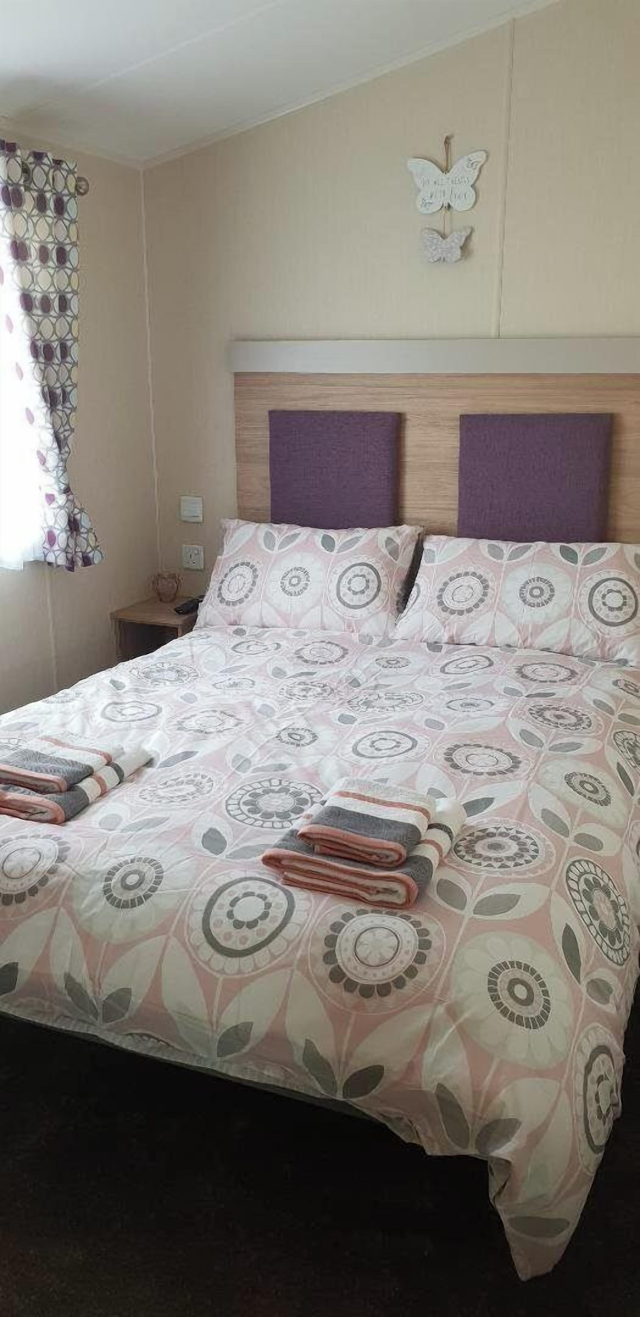 A neatly made bed with a patterned bedspread, two pillows, and folded towels.