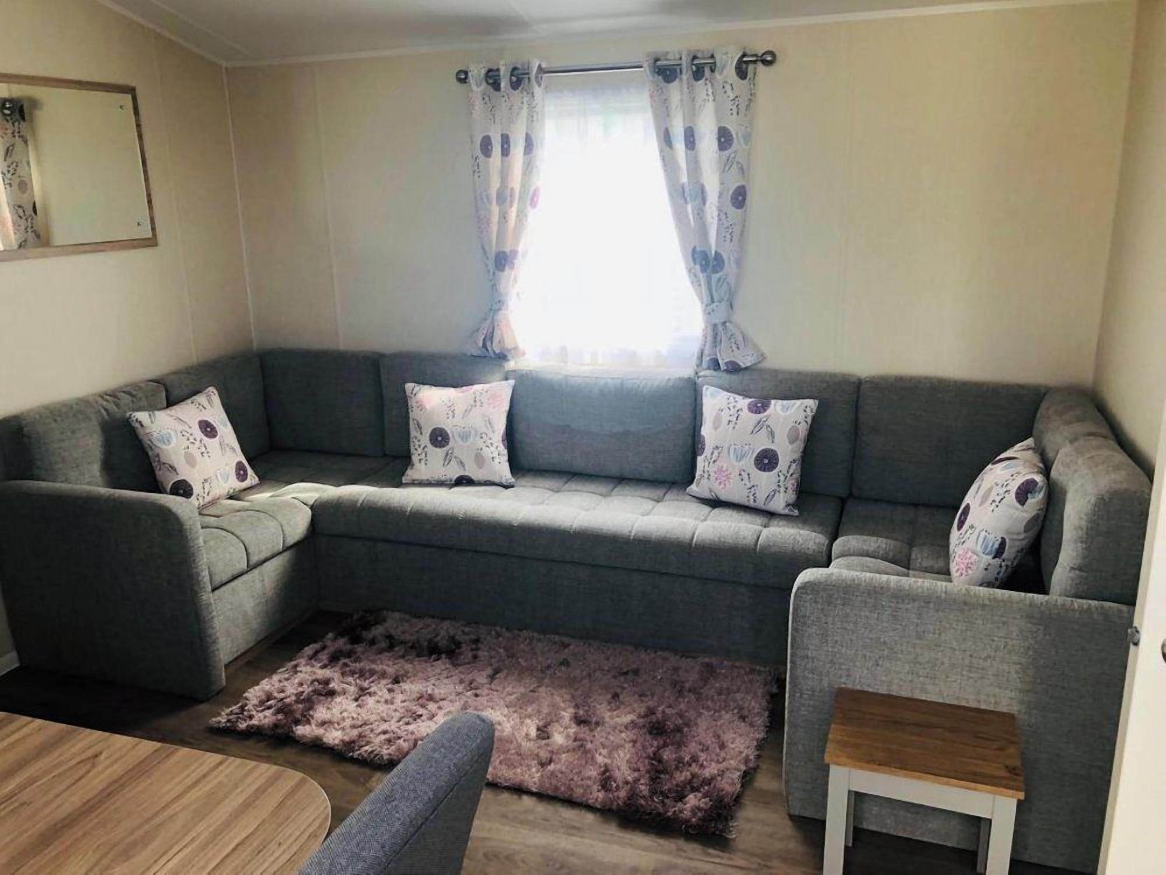 A grey sectional sofa with patterned cushions, a small wooden side table, and a fluffy rug.