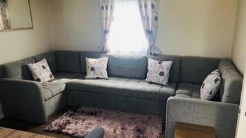 A grey sectional sofa with patterned cushions, a small wooden side table, and a fluffy rug.